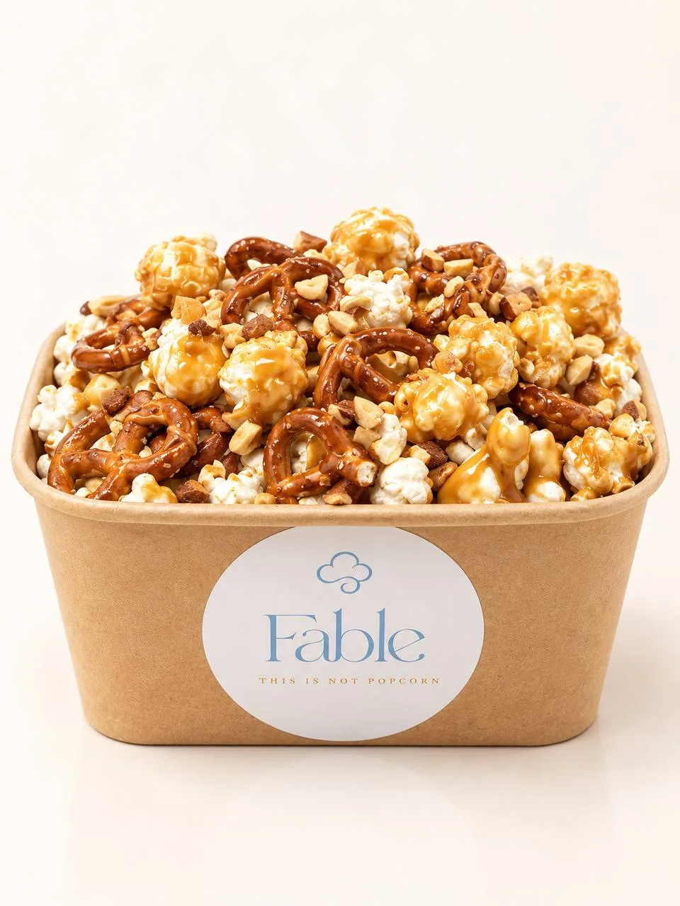 A large kraft Fable tub of Caramel Ever After popcorn, heaped high with a golden drizzle and pretzel twists.