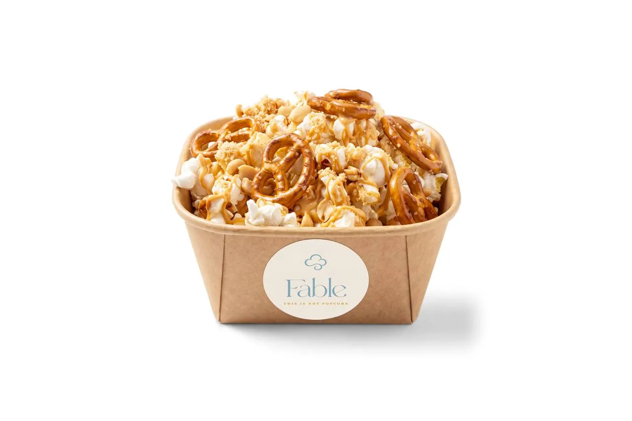 A kraft Fable tub of Caramel Ever After popcorn with a golden drizzle and pretzel twists, shown with the optional nuts.