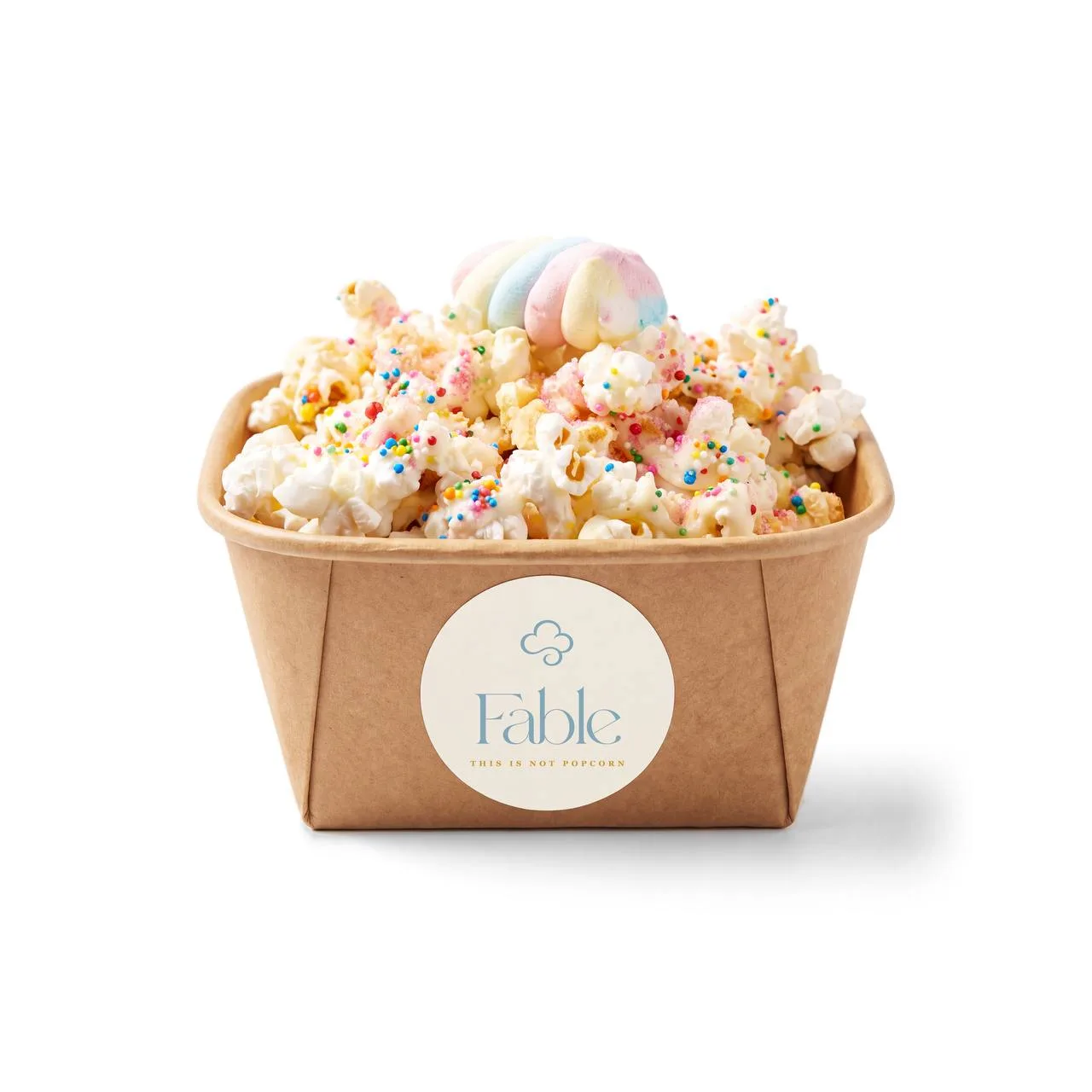 A kraft Fable tub of Unicorn Wishes popcorn with a creamy drizzle and rainbow sprinkles, crowned with a pastel swirl.