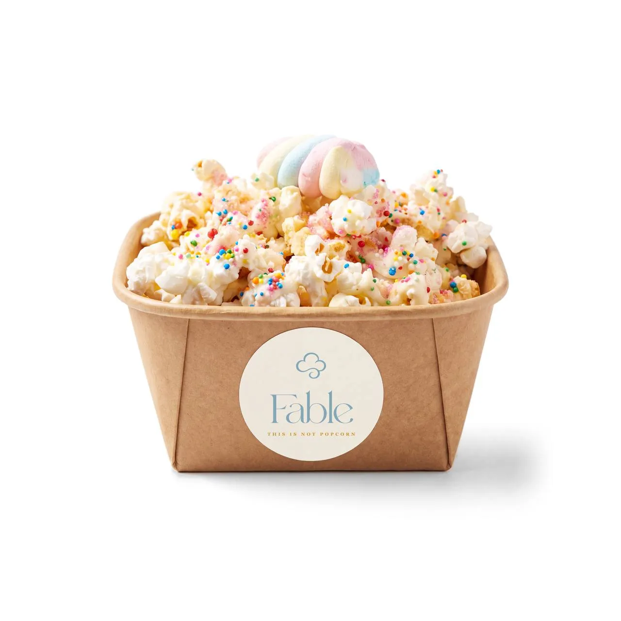A kraft Fable tub of Unicorn Wishes popcorn with a creamy drizzle and rainbow sprinkles, crowned with a pastel swirl.